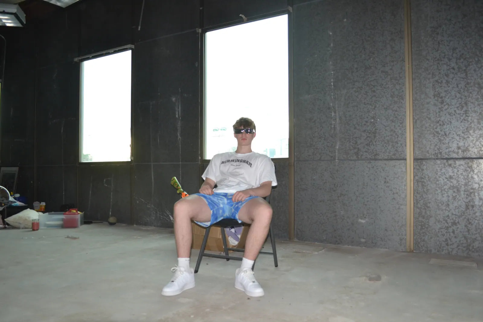 Carter Vail seated alone in an empty concrete room in the white tee and sunglasses