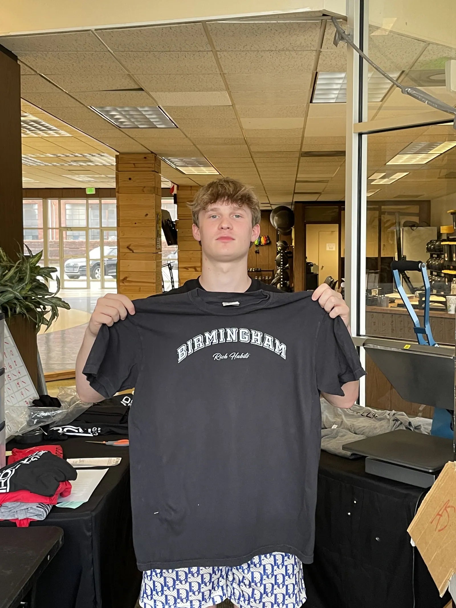 Carter Vail holding the black Birmingham tee in a print shop