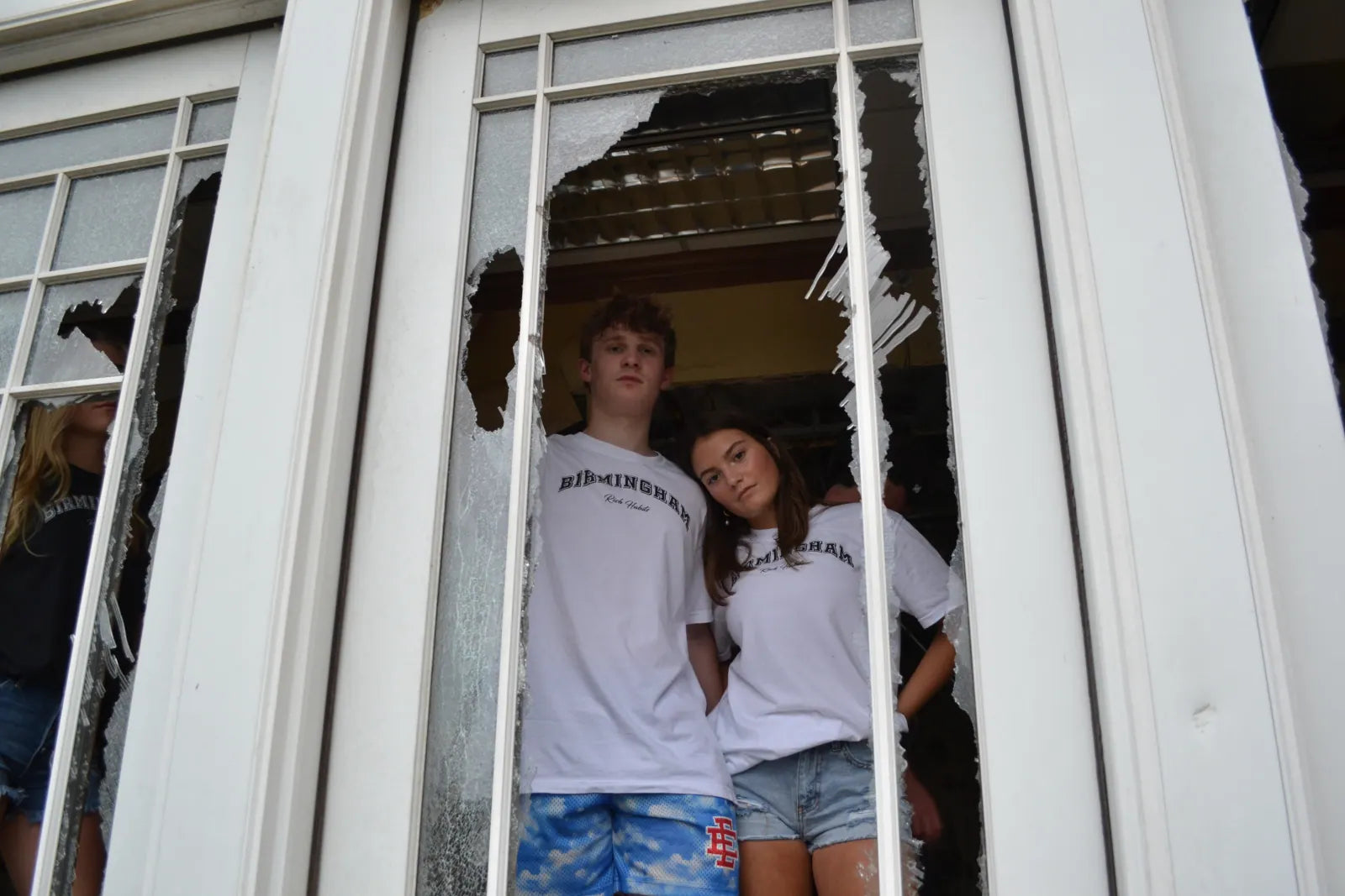 Carter and Sarah in matching white Birmingham tees framed by a broken window