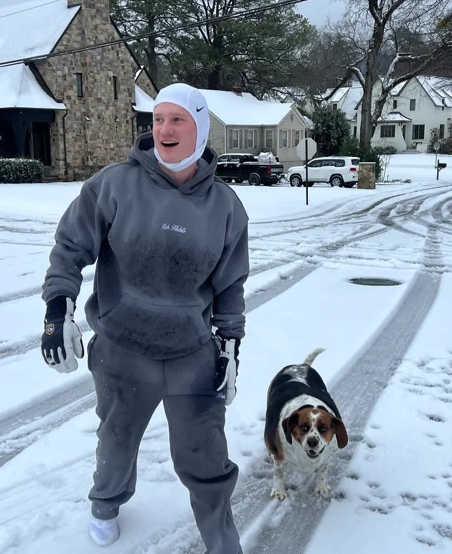 Carter Vail in a grey Rich Habits hoodie in the snow with his dog
