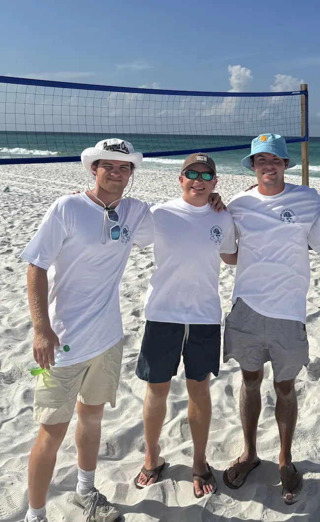 Sam Sutton, Charlie Reeves and their friend Will in white tees and bucket hats on the sand at church camp
