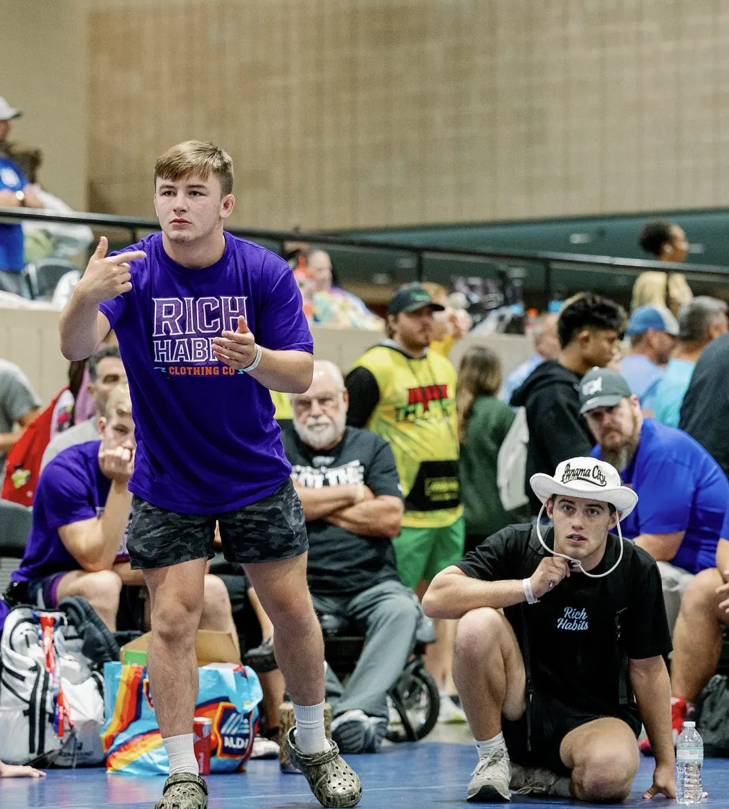Cory Land coaching in a purple Rich Habits tee while Sam Sutton kneels beside him in black