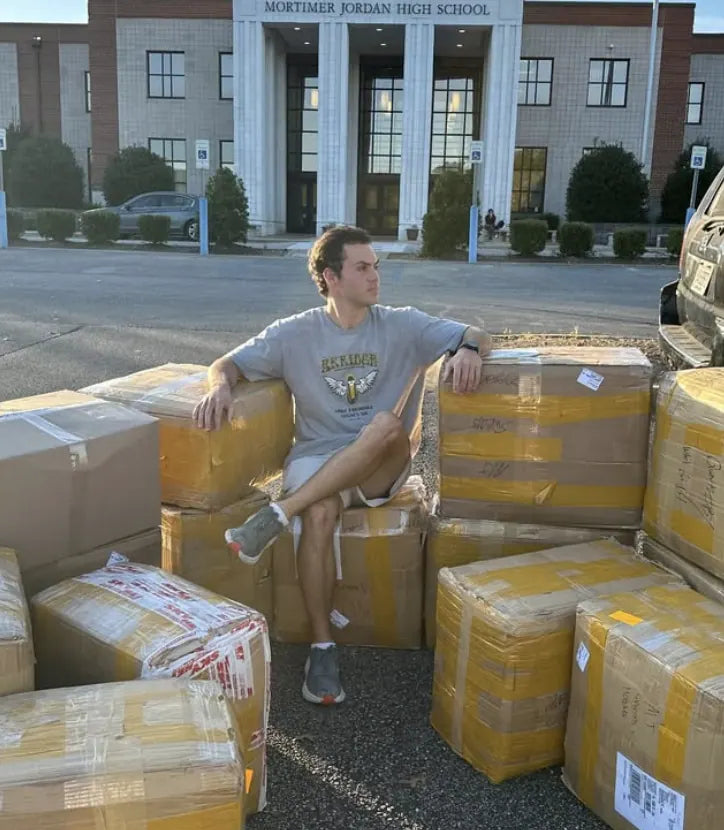 Charlie Reeves sitting on a wall of taped boxes in front of Mortimer Jordan High School