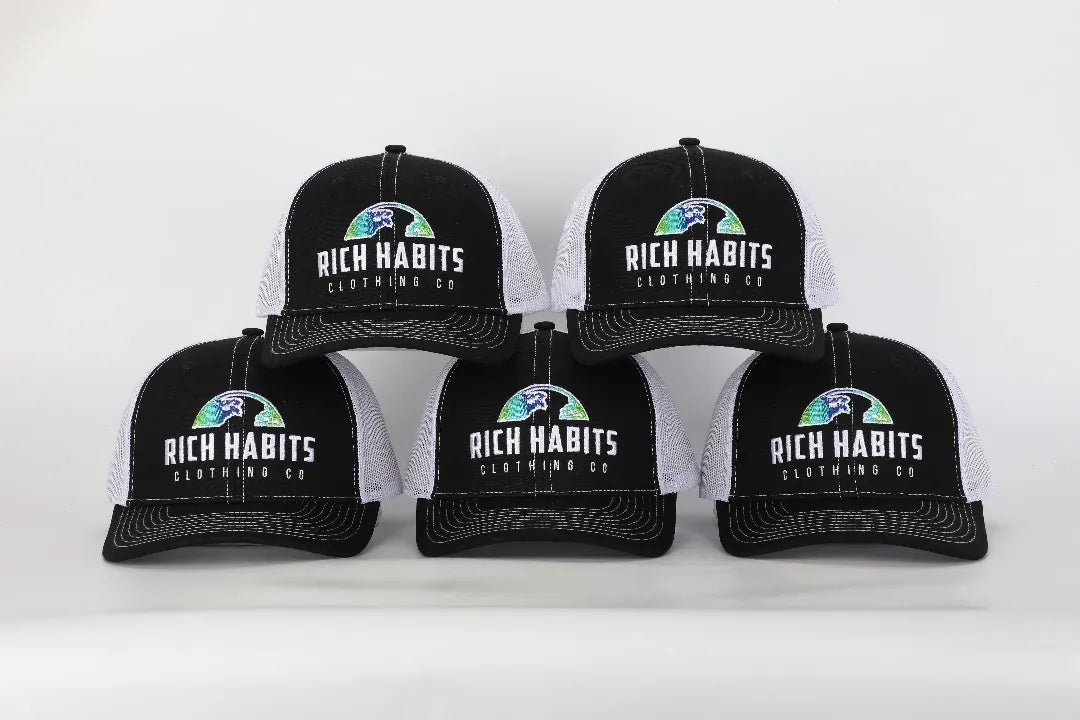 Five black and white Rich Habits trucker caps with the original globe logo on a white sweep