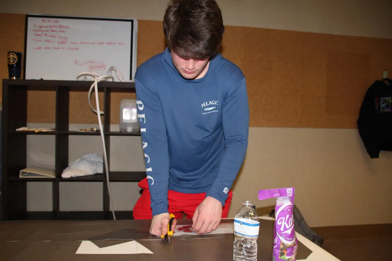 Sam Carr cutting prints, a to-do list on the whiteboard behind him