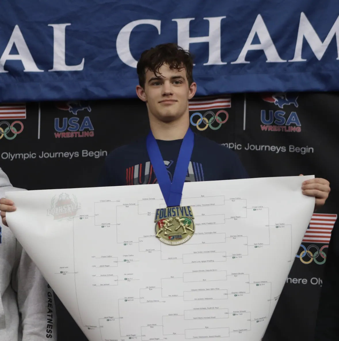 Sam Sutton with the gold medal and the Folkstyle Nationals bracket under the USA Wrestling banner