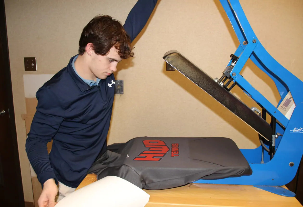 Sam Sutton at the blue heat press with a shirt on the platen