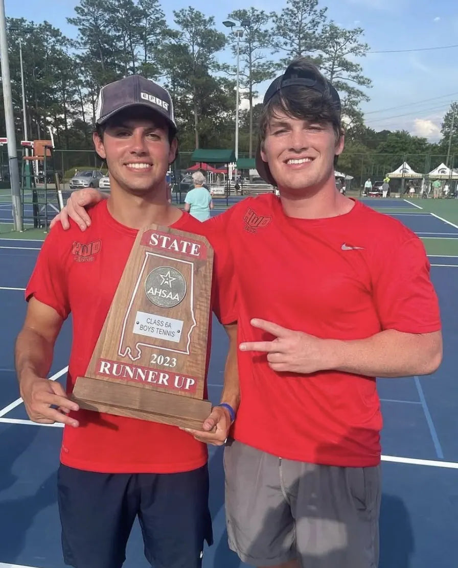 Charlie Reeves and Sam Carr holding the 2023 Class 6A state runner-up trophy in matching red Rich Habits tees