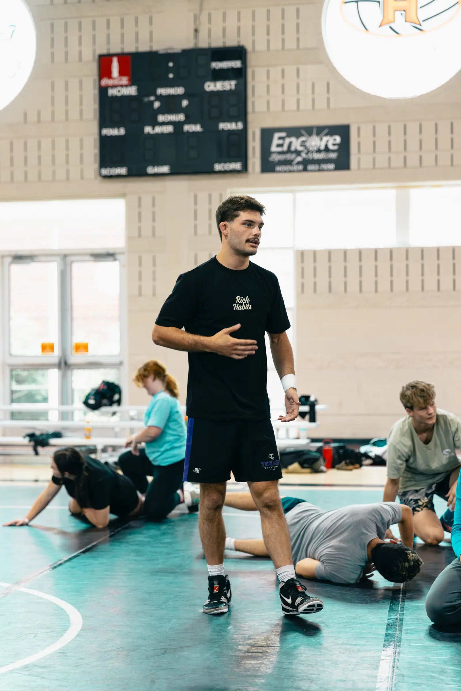 Ty Parker coaching a youth session on a wrestling mat in a Rich Habits tee