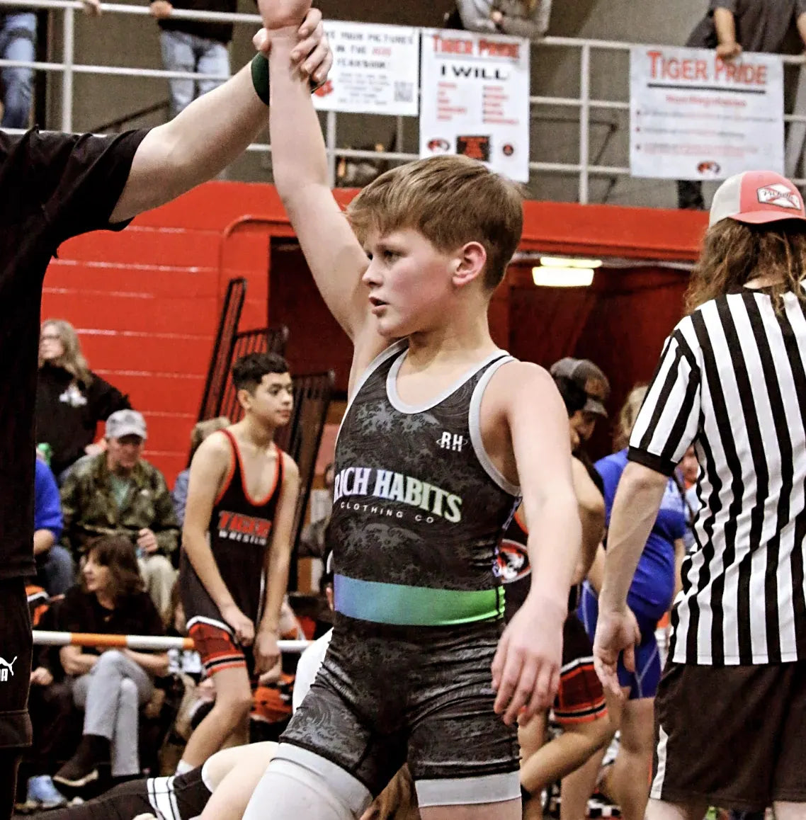 A youth wrestler getting his hand raised in a Rich Habits singlet
